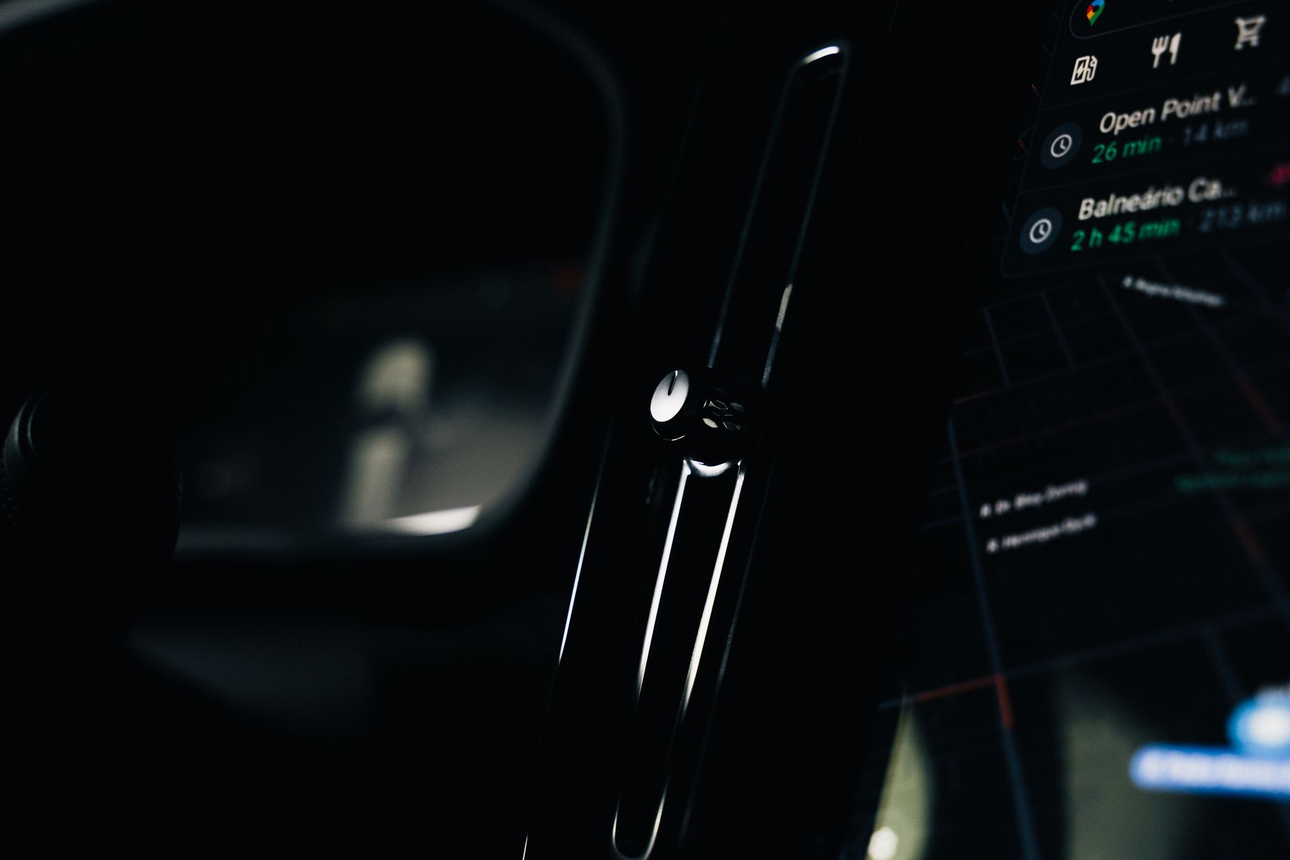 Intérieur sombre d’une voiture avec écran tactile de navigation à droite et bouche d’aération verticale au centre.